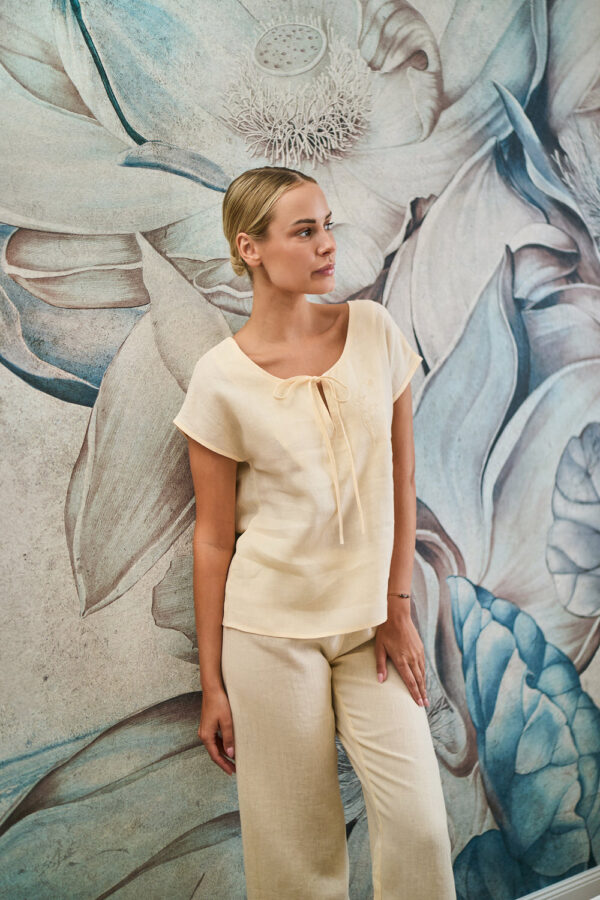 Kobieta w kremowym lnianym komplecie stojąca na tle ściany z wielkoformatową kwiatową tapetą