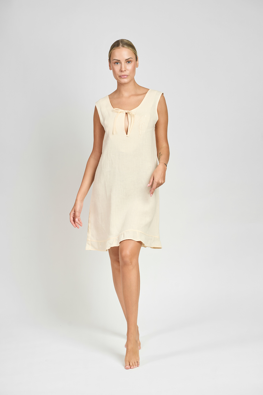 Kobieta w kremowej koszuli nocnej z delikatnym wiązaniem przy dekolcie, idąca na jasnym tle