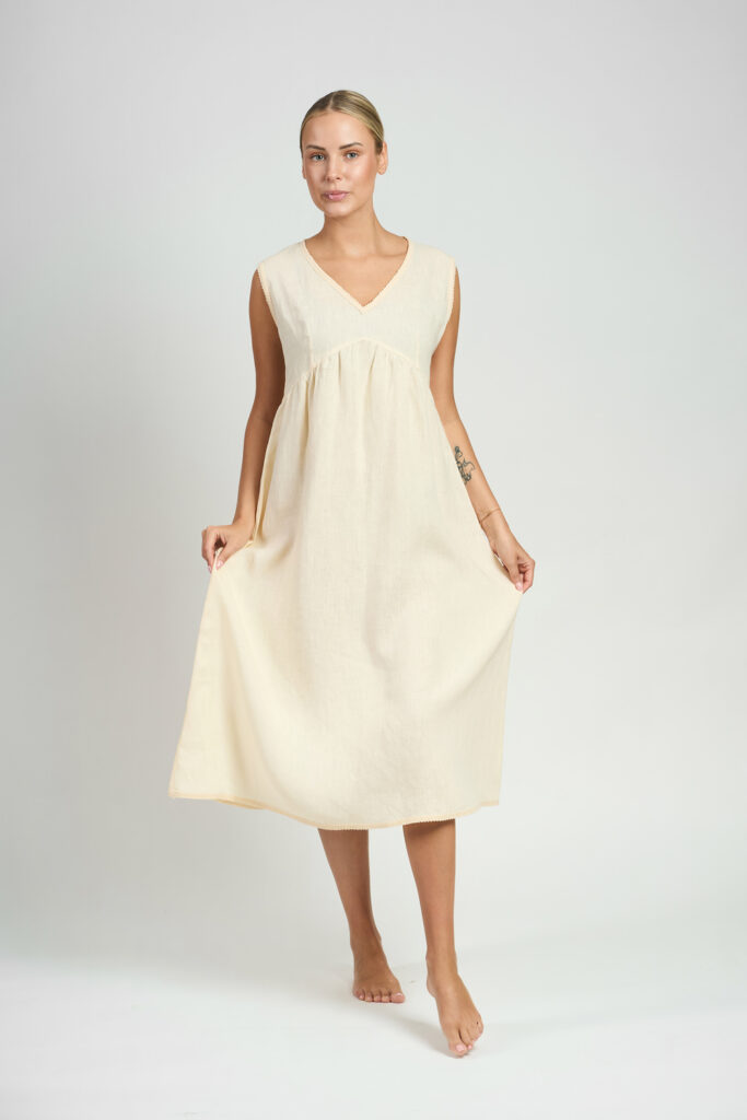 Kobieta w kremowej koszuli nocnej o luźnym kroju trzymająca materiał po bokach