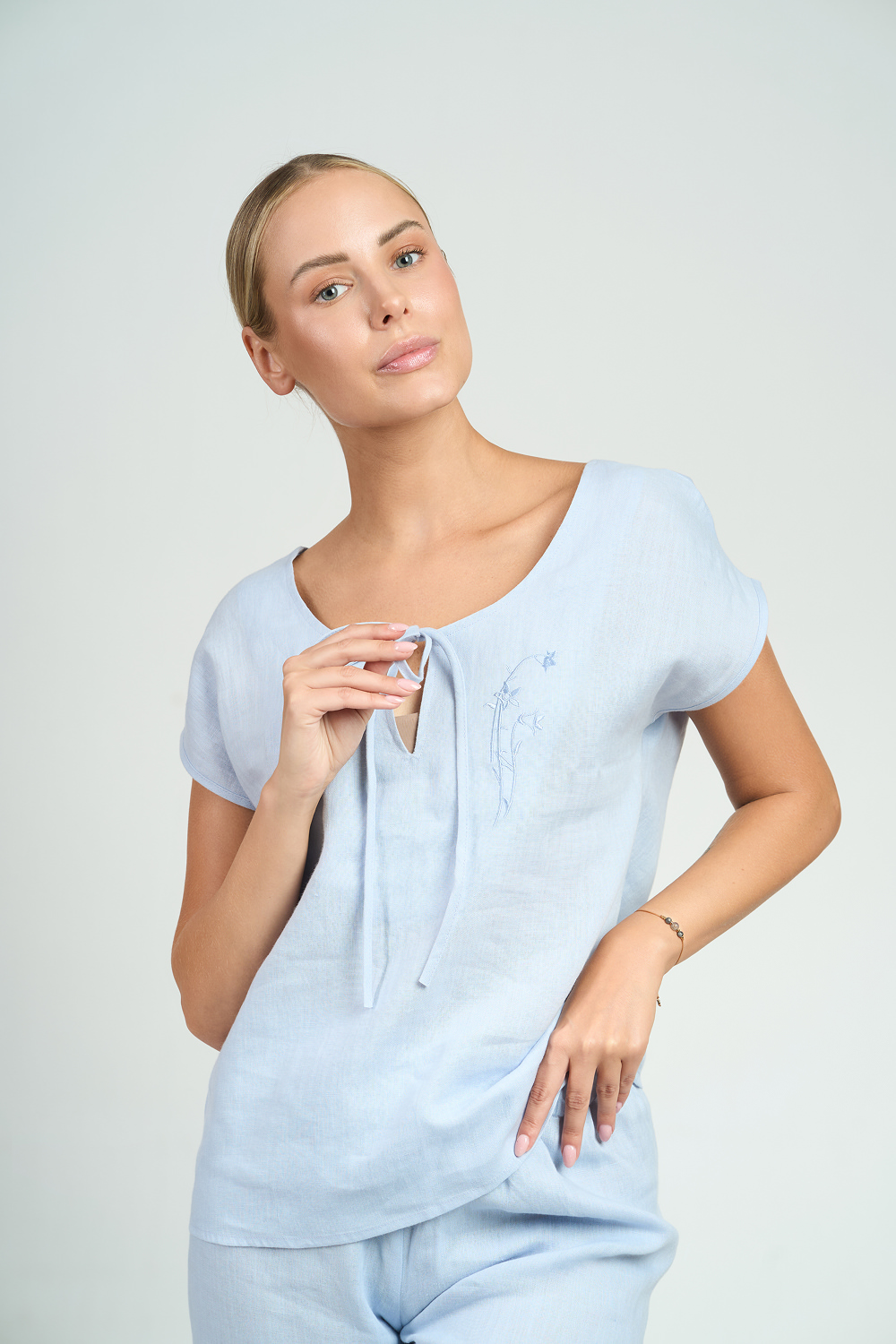 "Zbliżenie na błękitną lnianą bluzkę z wiązaniem i delikatnym haftem przy dekolcie