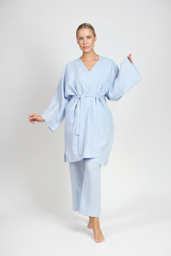 Kobieta w błękitnym lnianym komplecie z luźną bluzką z paskiem i szerokimi spodniami