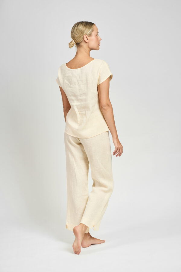 spodnie-lniane-waniliowy-sen-dreamairy-02 Kobieta w kremowym lnianym komplecie widziana od tyłu, z bluzką z krótkim rękawem