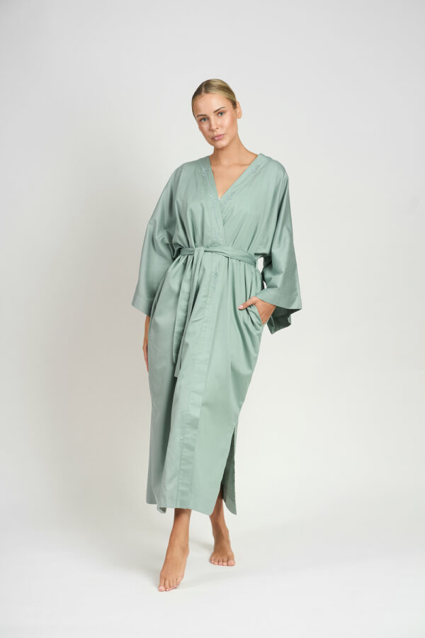 Kobieta w długim szałwiowym szlafroku z ręką w kieszeni, stojąca na jasnym tle