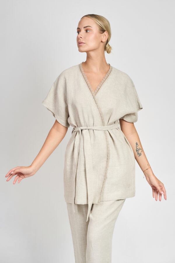 Kobieta w beżowym lnianym kimonie z wiązaniem w talii i ozdobnym wykończeniem przy dekolcie