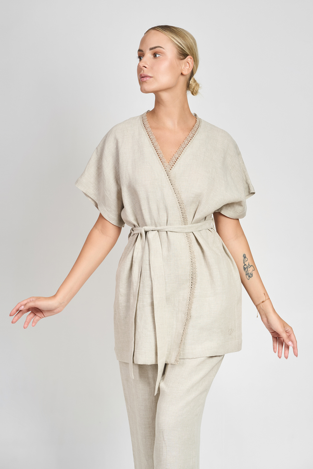 Kobieta w beżowym lnianym kimonie z wiązaniem w talii i ozdobnym wykończeniem przy dekolcie